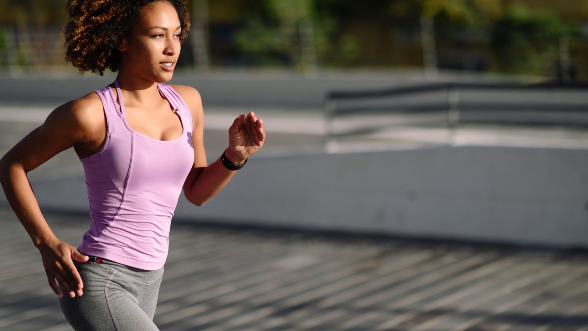 Woman in pink tank top and grey leggings out for a jog.