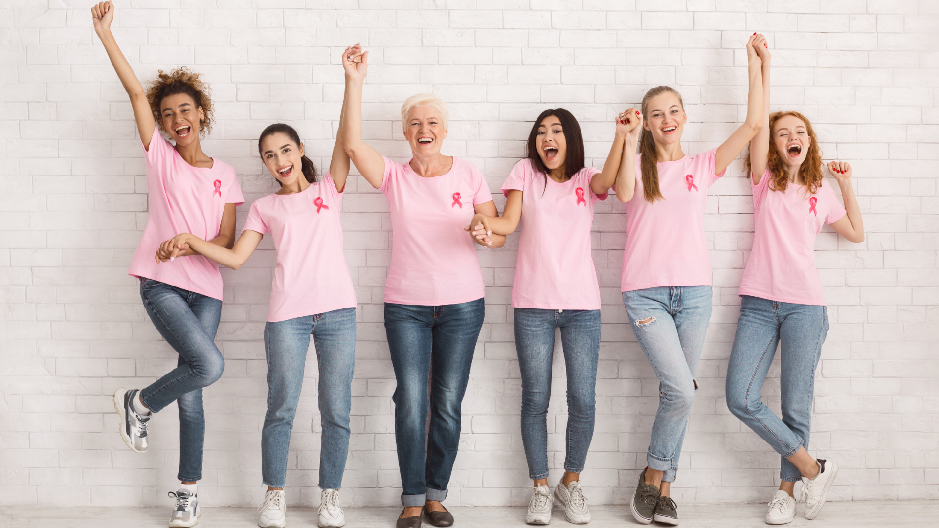 Group of women wearing pink shirts and breast cancer ribbons celebrating strength and survivorship together.