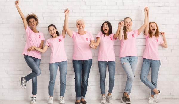 Group of women wearing pink shirts and breast cancer ribbons celebrating strength and survivorship together.