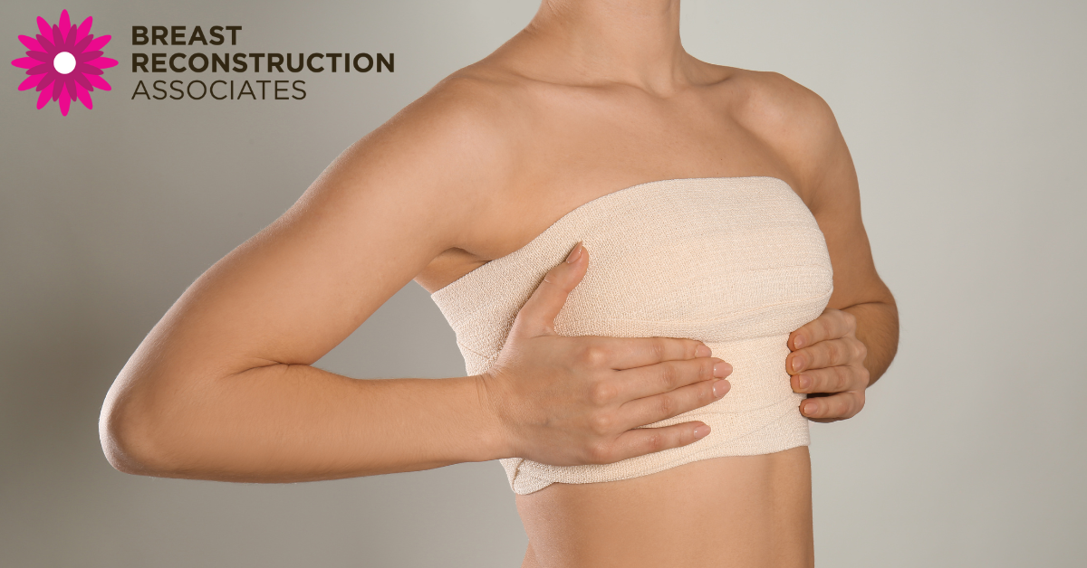 woman with a bandaged chest after breast reconstruction surgery, gently holding her breasts for support. Image includes the Breast Reconstruction Associates logo.