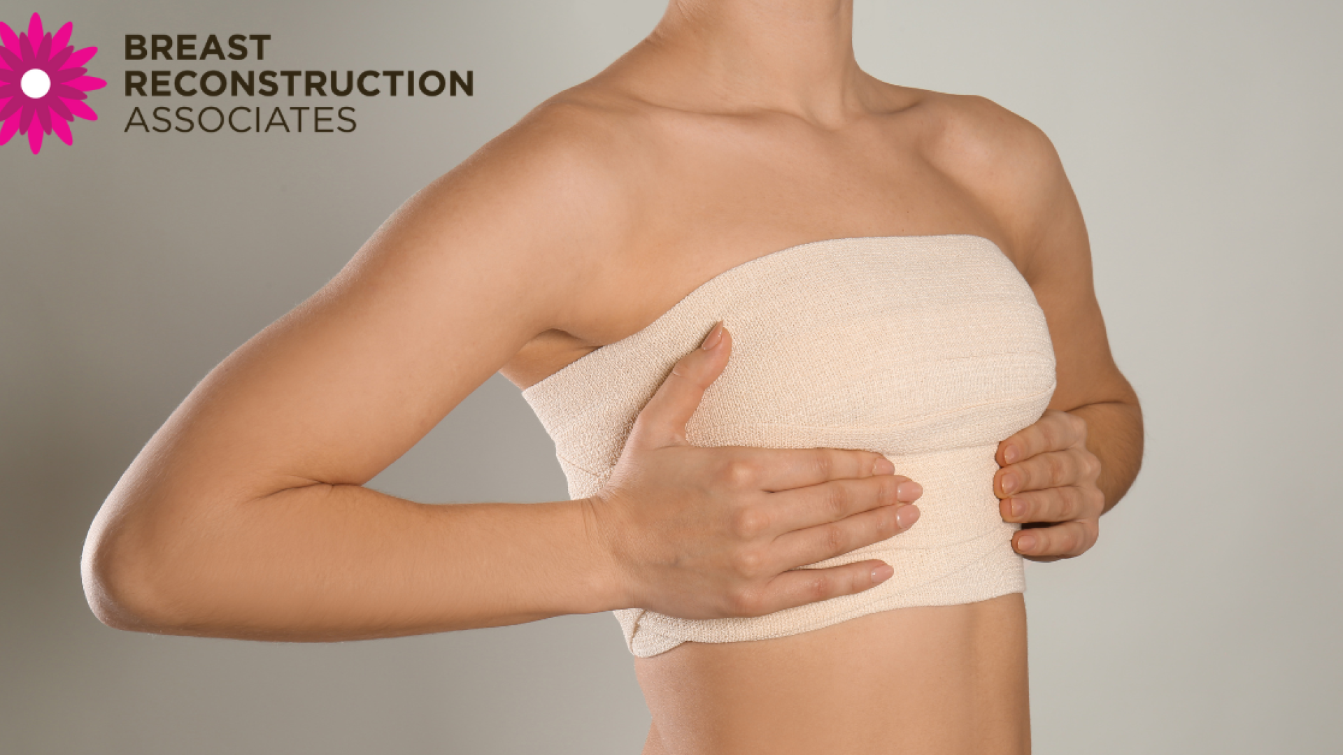 woman with a bandaged chest after breast reconstruction surgery, gently holding her breasts for support. Image includes the Breast Reconstruction Associates logo.